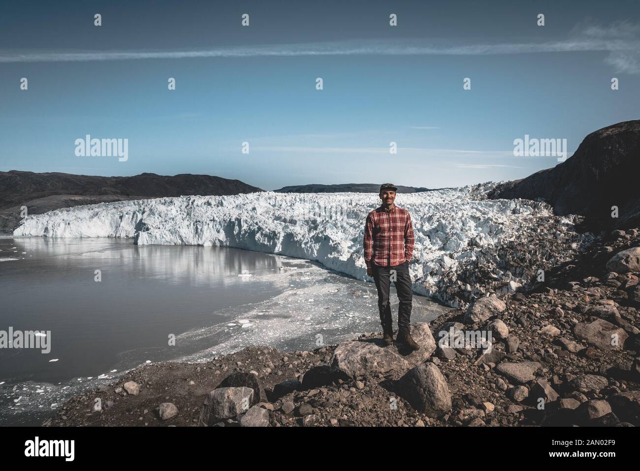 Ein junger Mann reisender Tourist vor Eqip Sermia Gletscher Eqi Gletscher genannt. Wand aus Eis im Hintergrund. Das Konzept der globalen Erwärmung und der Stockfoto