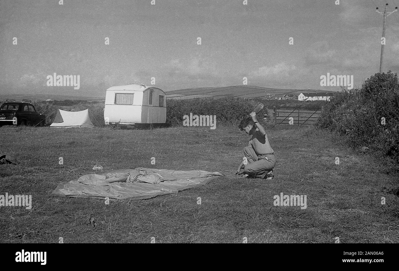 1950, historische, Camping, ein junger Mann, der in einem Feld unten kniend auf dem Gras über eine Leinwand Zelt zu setzen. Stockfoto