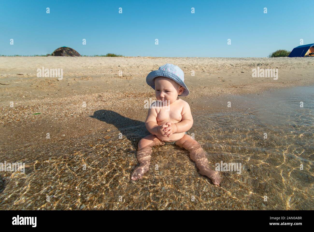 Kleine Mädchen in einen Hut sitzt auf dem Ufer des Meeres im Wasser am Strand. Stockfoto