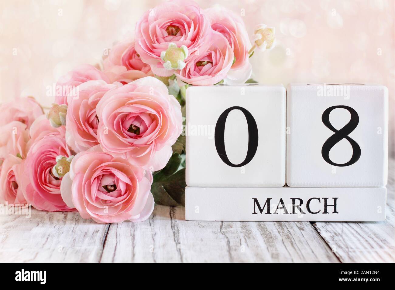 Weißes Holz Kalender Blöcke mit Datum März 08 für den Internationalen Tag der Frau und Rosa ranunkeln Blumen über einen hölzernen Tisch. Stockfoto