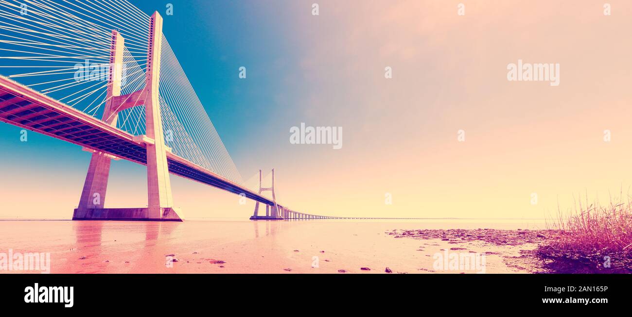 Lissabon, Portugal. Bunte Straßenfotografie. Malerische Landschaft und Tourismus.Vasco da Gama Brücke über den Tejo bei Sonnenuntergang mit Sonne und Wolken. Stockfoto