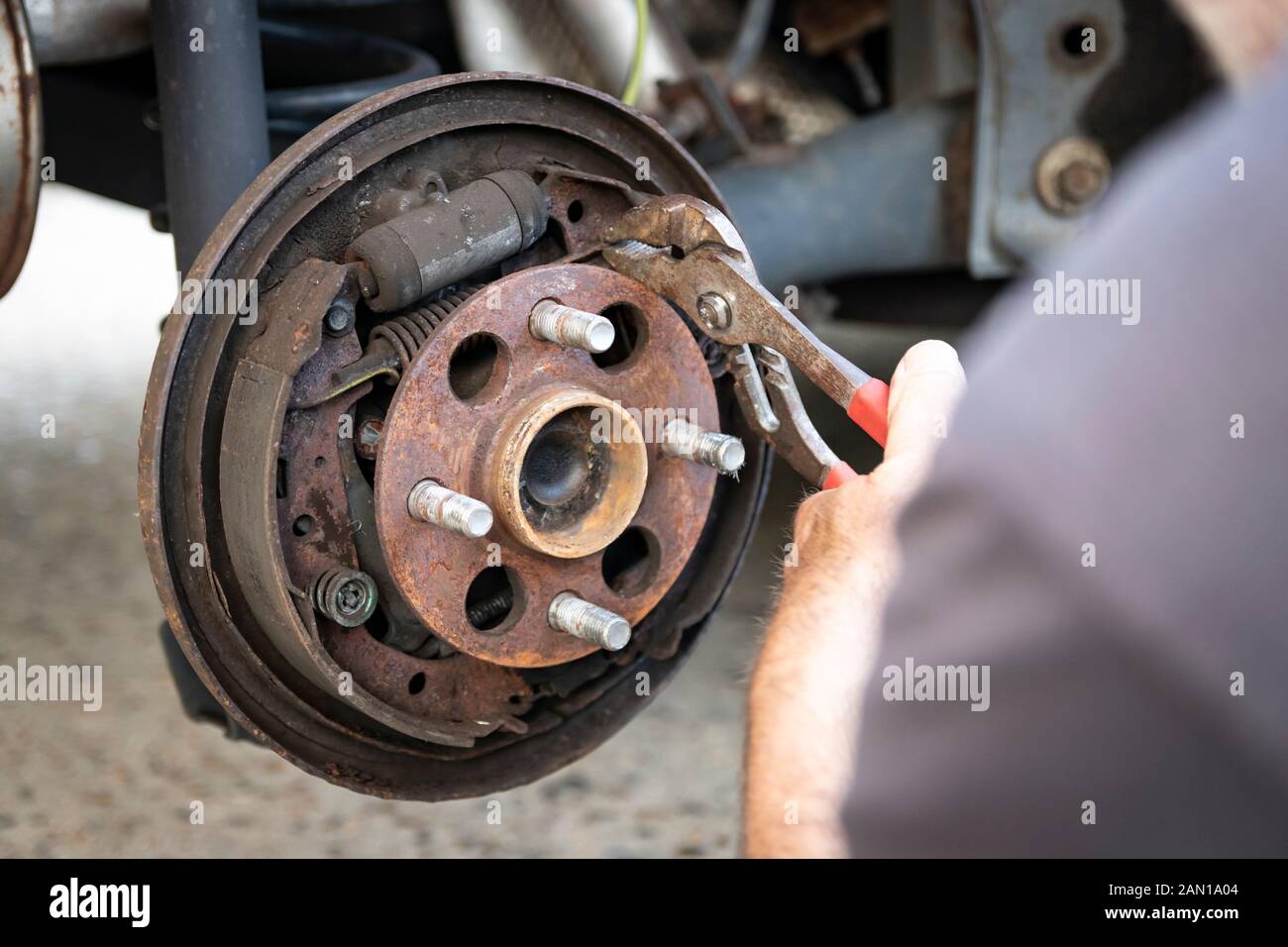 Mann mit einer Zange arbeitet auf freiliegenden Auto Bremsen während Bremsbeläge job Stockfoto