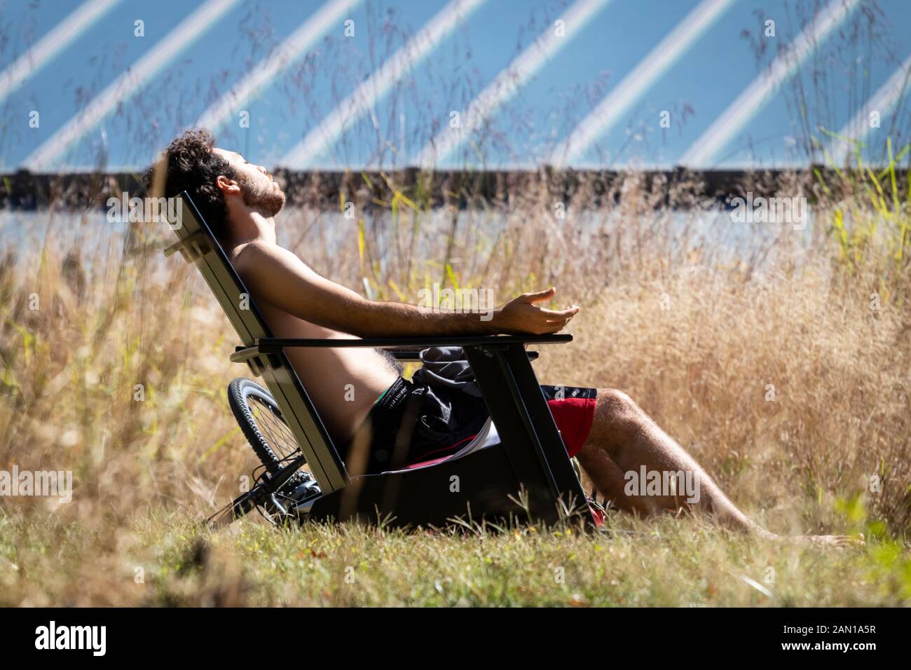 Mann mit Bart sitzt Bräunen in Rasen Stuhl und saugt die Sonne, in der Nähe von großen Solaranlagen Stockfoto