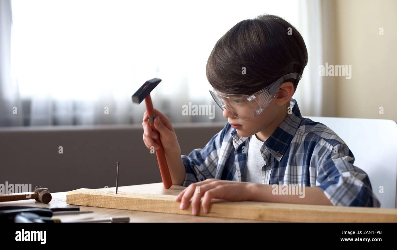 Niedlicher kleiner Junge, der Nagel in Holzpflaster, Hobby und Freizeit hämmert, Werkstatt Stockfoto