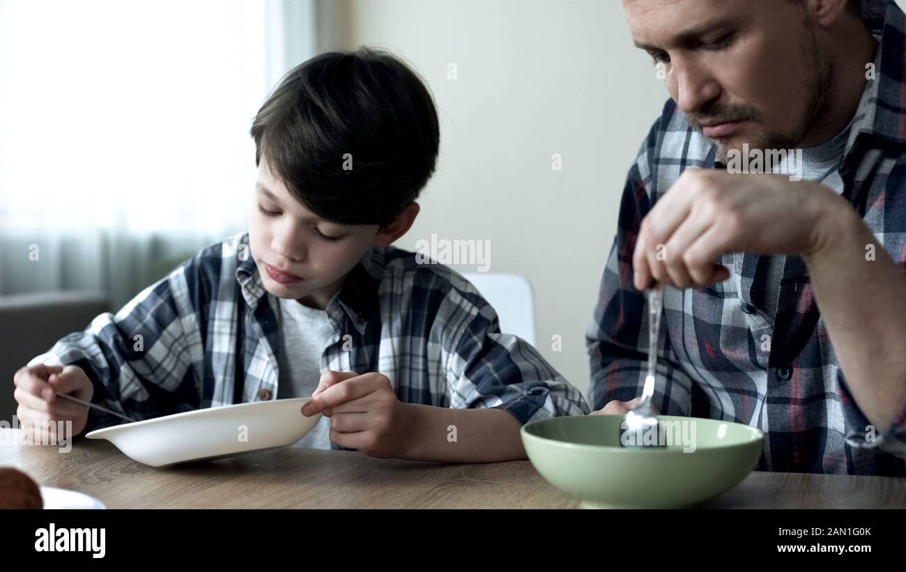 Ernst alleinerziehender Vater und sein Sohn essen morgens Cornflakes, schlechtes Frühstück Stockfoto