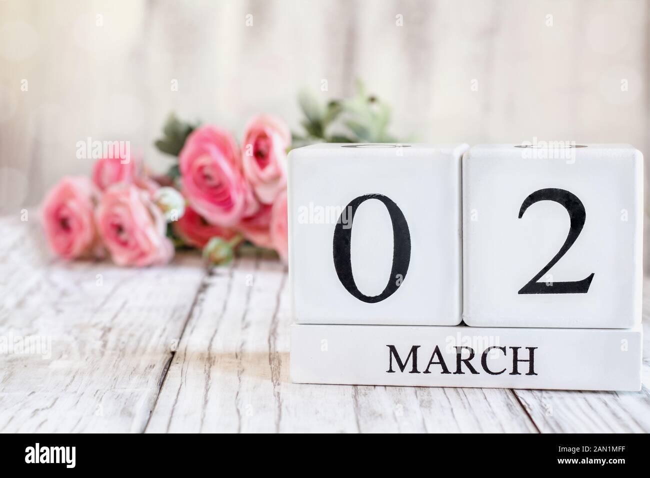 Weißes Holz Kalender Blöcke mit Datum März 02. Selektiver Fokus mit rosa Ranunkeln im Hintergrund über einen hölzernen Tisch. Stockfoto