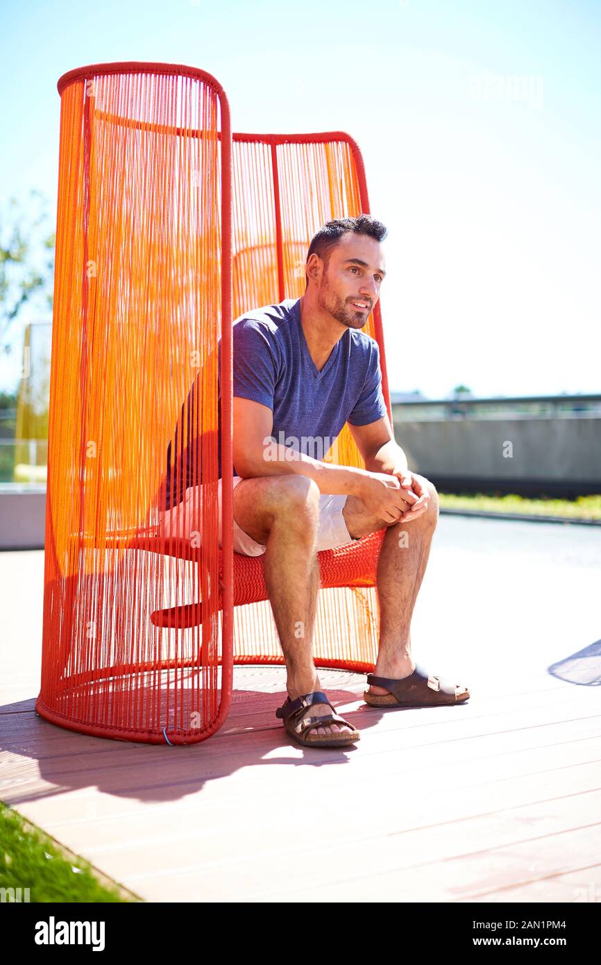 Ein Mann, der draußen in einem bunten modernen Stuhl sitzt. Stockfoto