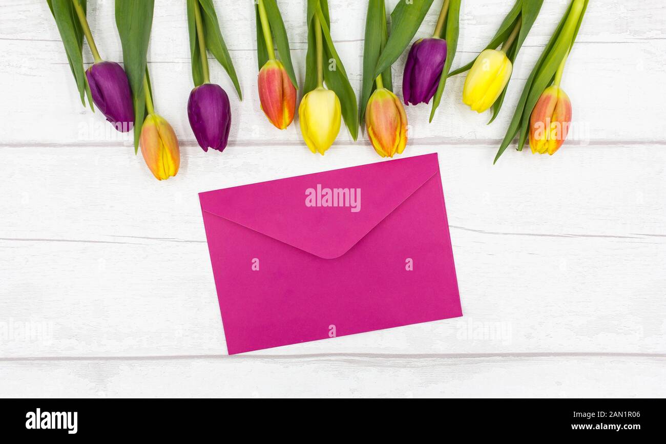 Blick von oben auf die schöne, bunte/Bunte Tulpen und Rosa Umschlag auf einem weißen Tisch im Landhausstil - Muttertag/Valentinstag Anzeige Stockfoto