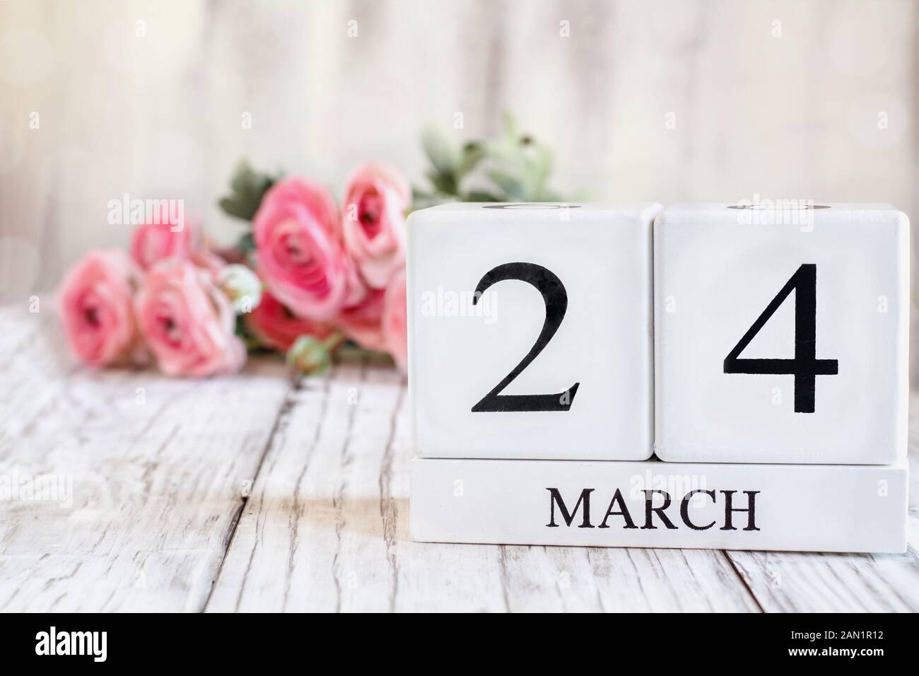 Weißes Holz Kalender Blöcke mit dem Datum 24. März. Selektiver Fokus mit rosa Ranunkeln im Hintergrund über einen hölzernen Tisch. Stockfoto