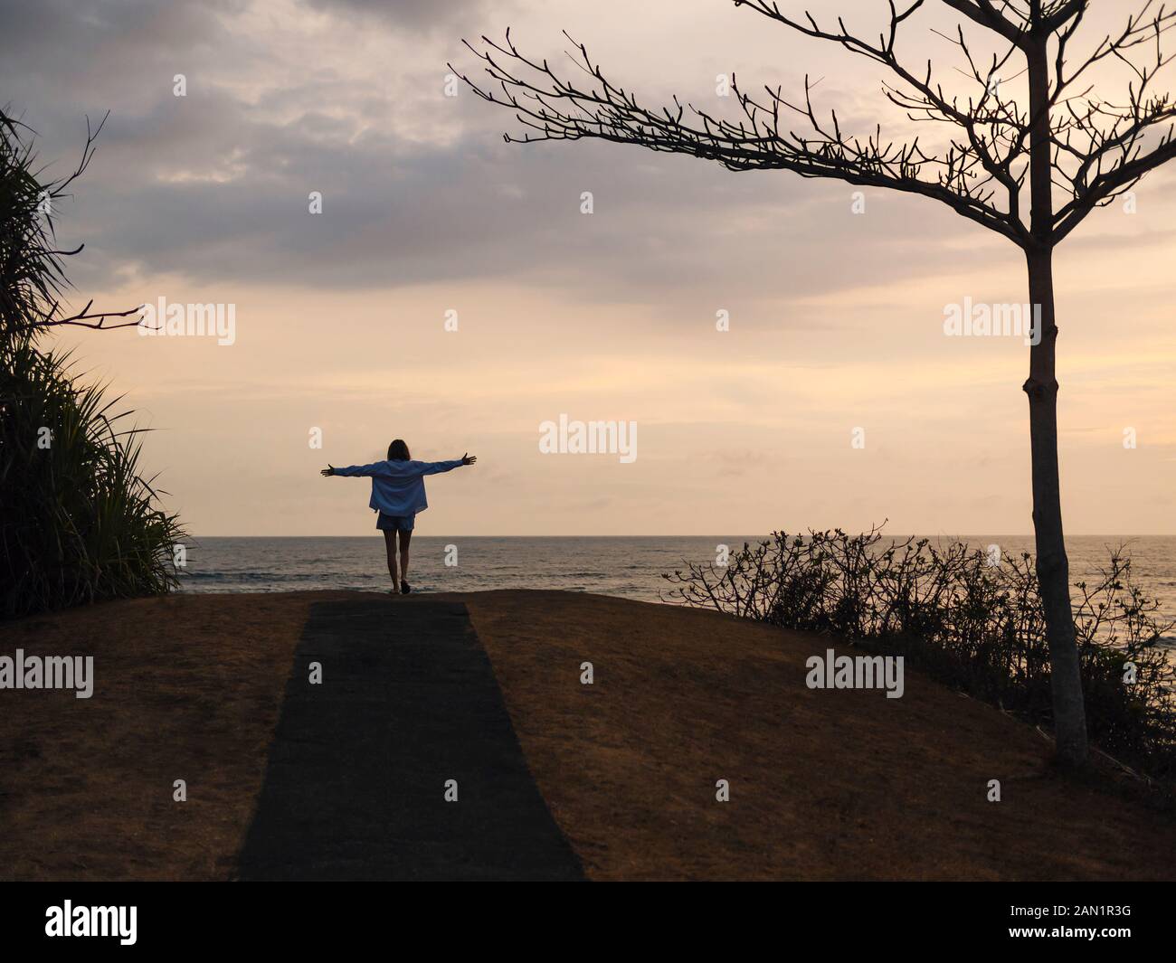 Frau mit erhobenen Armen, die bei Sonnenuntergang am Meer steht Stockfoto