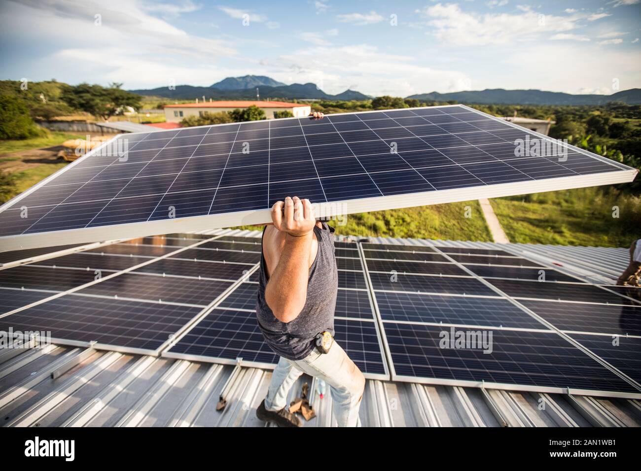 Starker Bauarbeiter trägt Solarpanel über Kopf auf Dach. Stockfoto