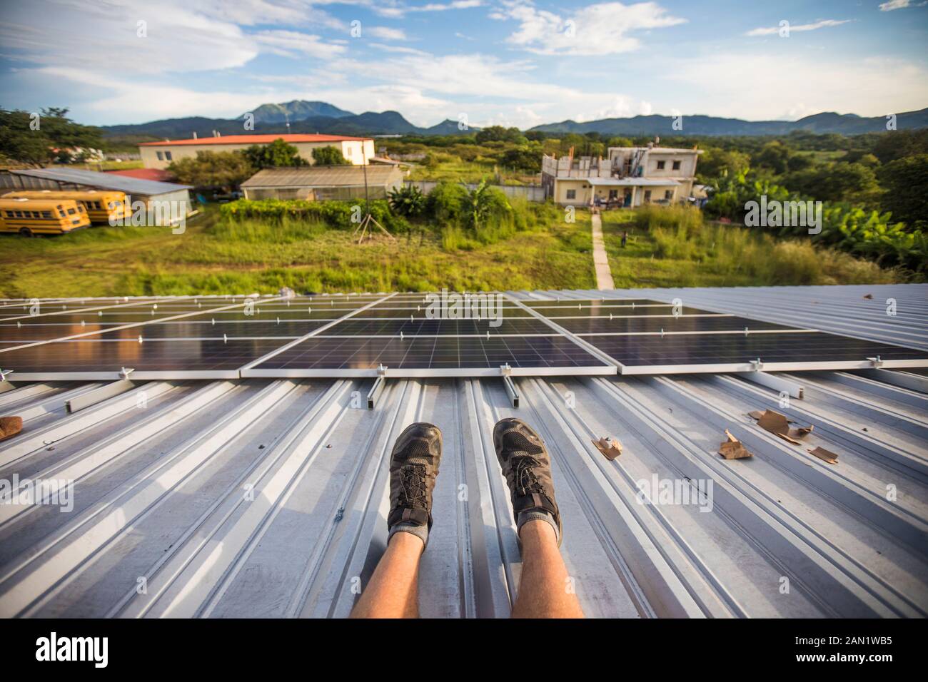 Hohe Winkelansicht der Beine der Arbeiter und installierte Solarpaneele vom Dach. Stockfoto
