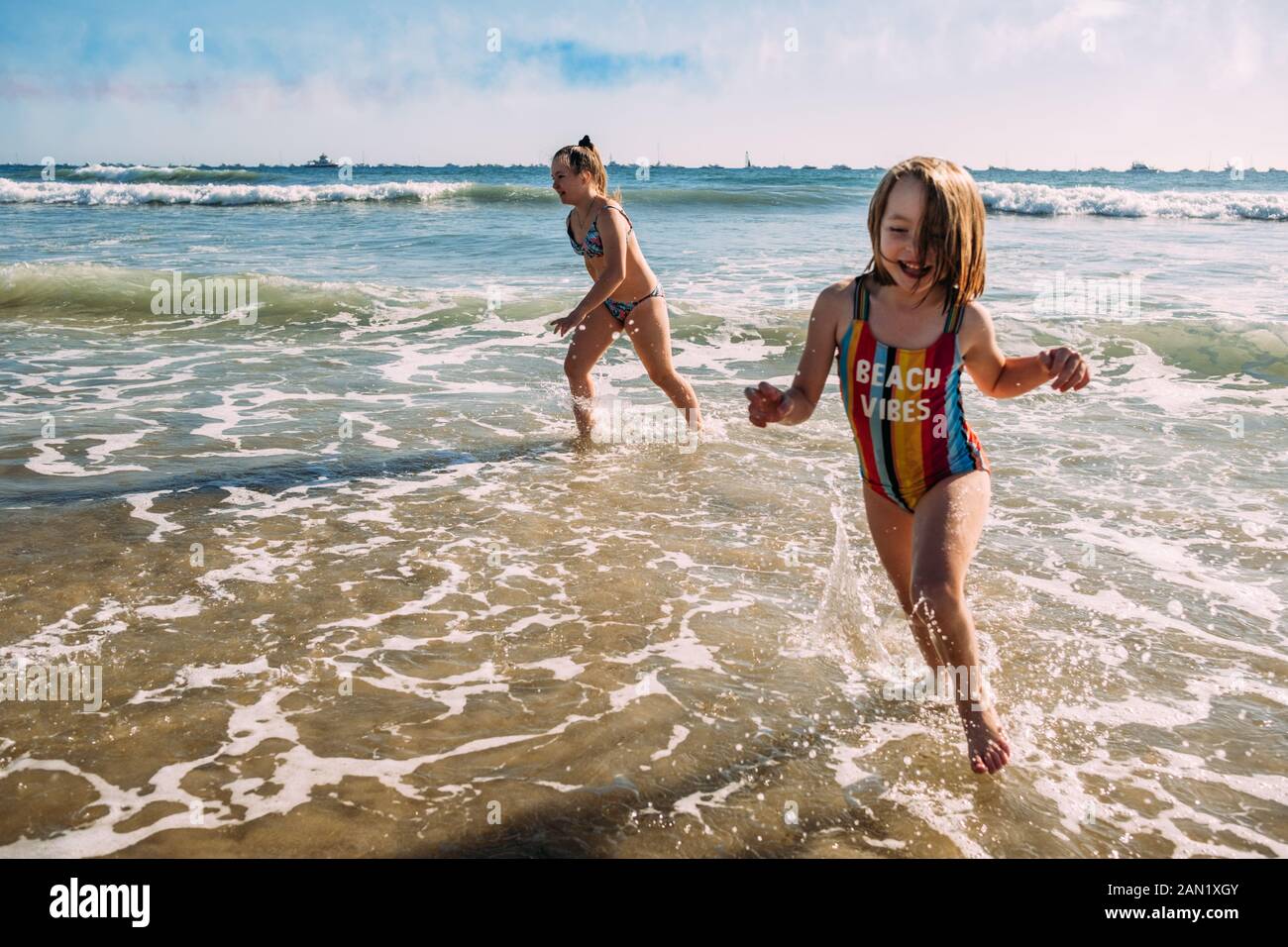 Schwestern, die am Strand laufen und im Wasser planschen Stockfoto