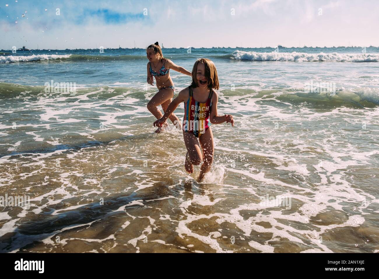 Geschwister, die an einem sonnigen Tag im Wasser am Strand laufen Stockfoto