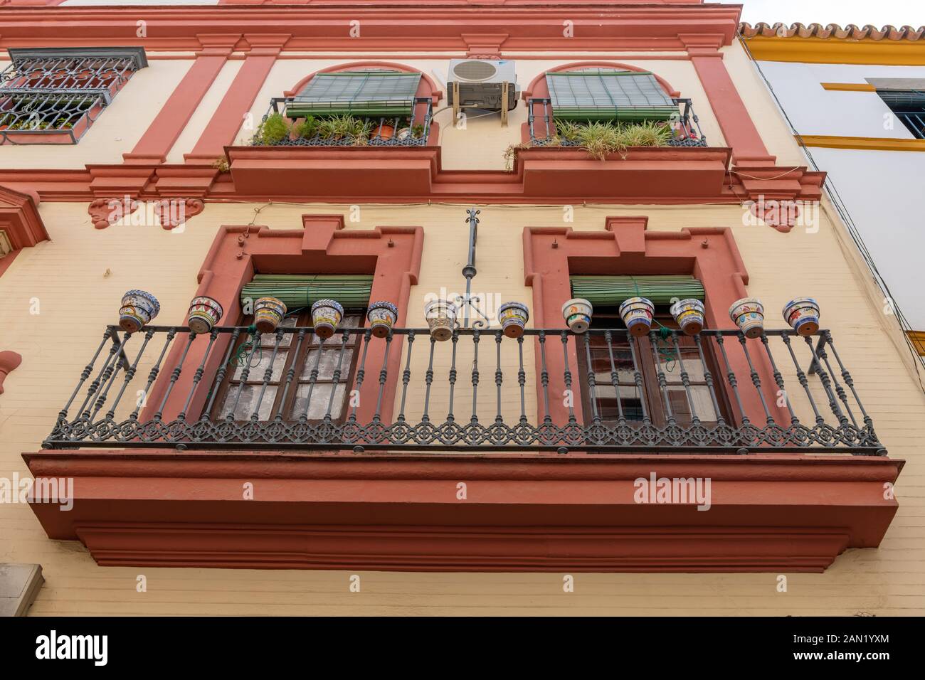 Eine Reihe dekorierter Keramikpflanzen-Töpfe auf einem schmiedeeisernen Balkon in einem farbenfrohen Apartmentblock in Sevilla Stockfoto