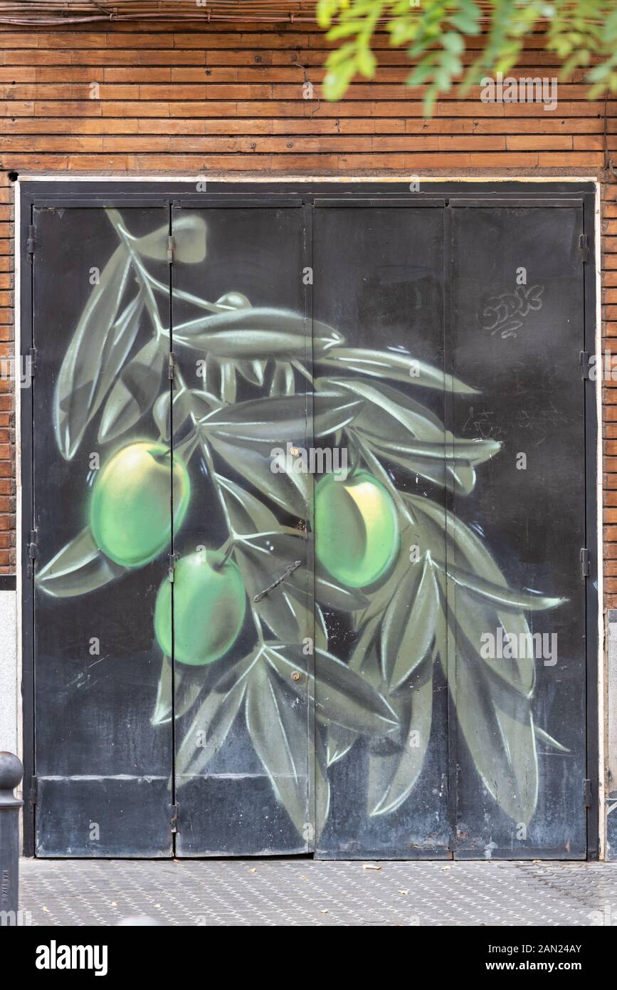 Ein Olivenzweig mit großen grünen Oliven, die auf der Garagentür eines Gebäudes auf der Plaza San Juan de la Palma in Sevilla gemalt wurden. Stockfoto