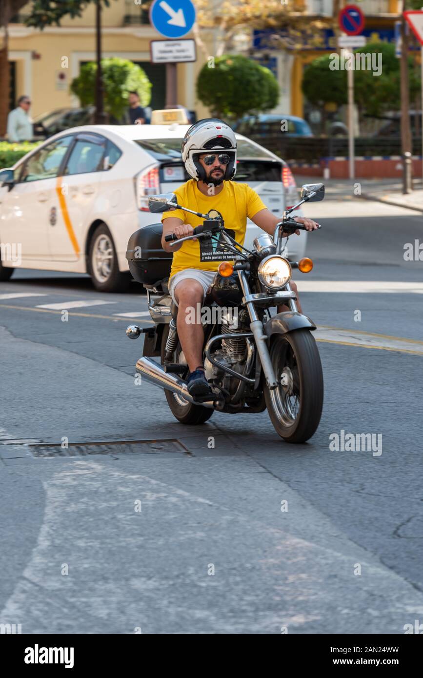 Ein bunter Biker in einem leuchtend gelben T-Shirt und Shorts fährt entlang der Calle Imagen. Sein Logo fordert weniger Atomraketen und mehr Kabeljau-Kracher! Stockfoto