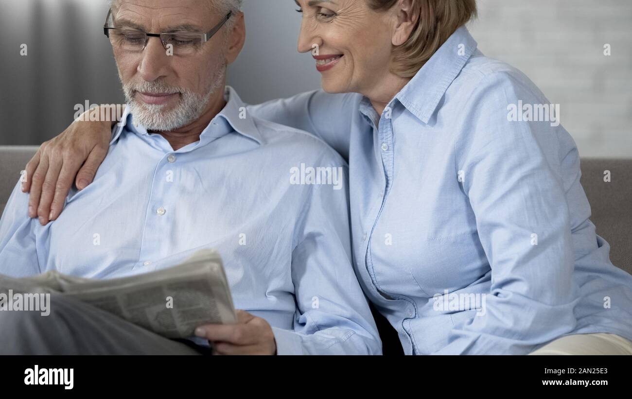 Rentner mann lesen Zeitung auf Sofa, Frau neben ihn umarmen, Liebe Stockfoto