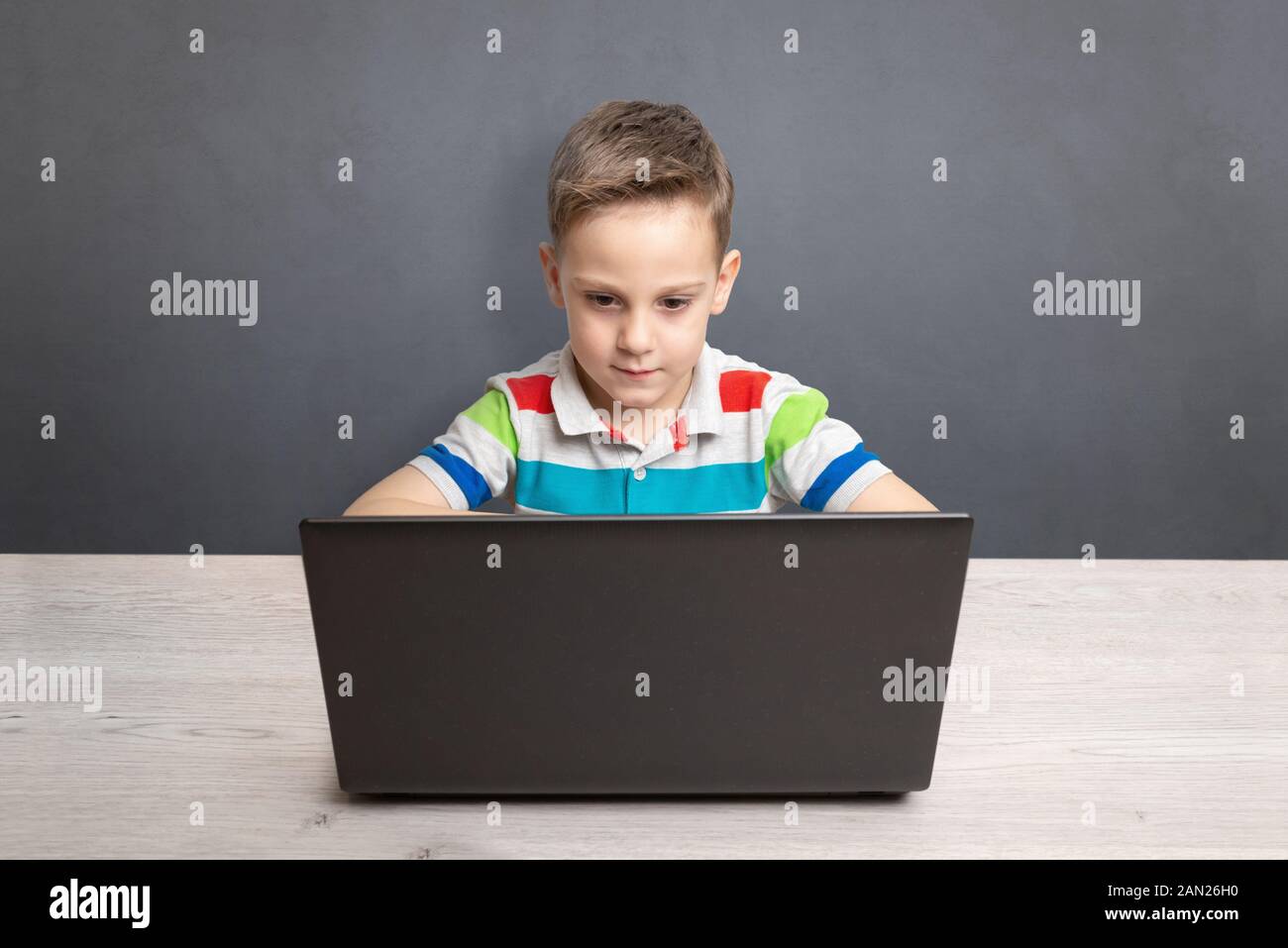 Junge arbeitet auf einem Laptop und einem Schreibtisch. Konzept der Computer zum Spielen und Lernen. Vorderansicht. Saubere Wände mit Platz für Text in backgroun Stockfoto