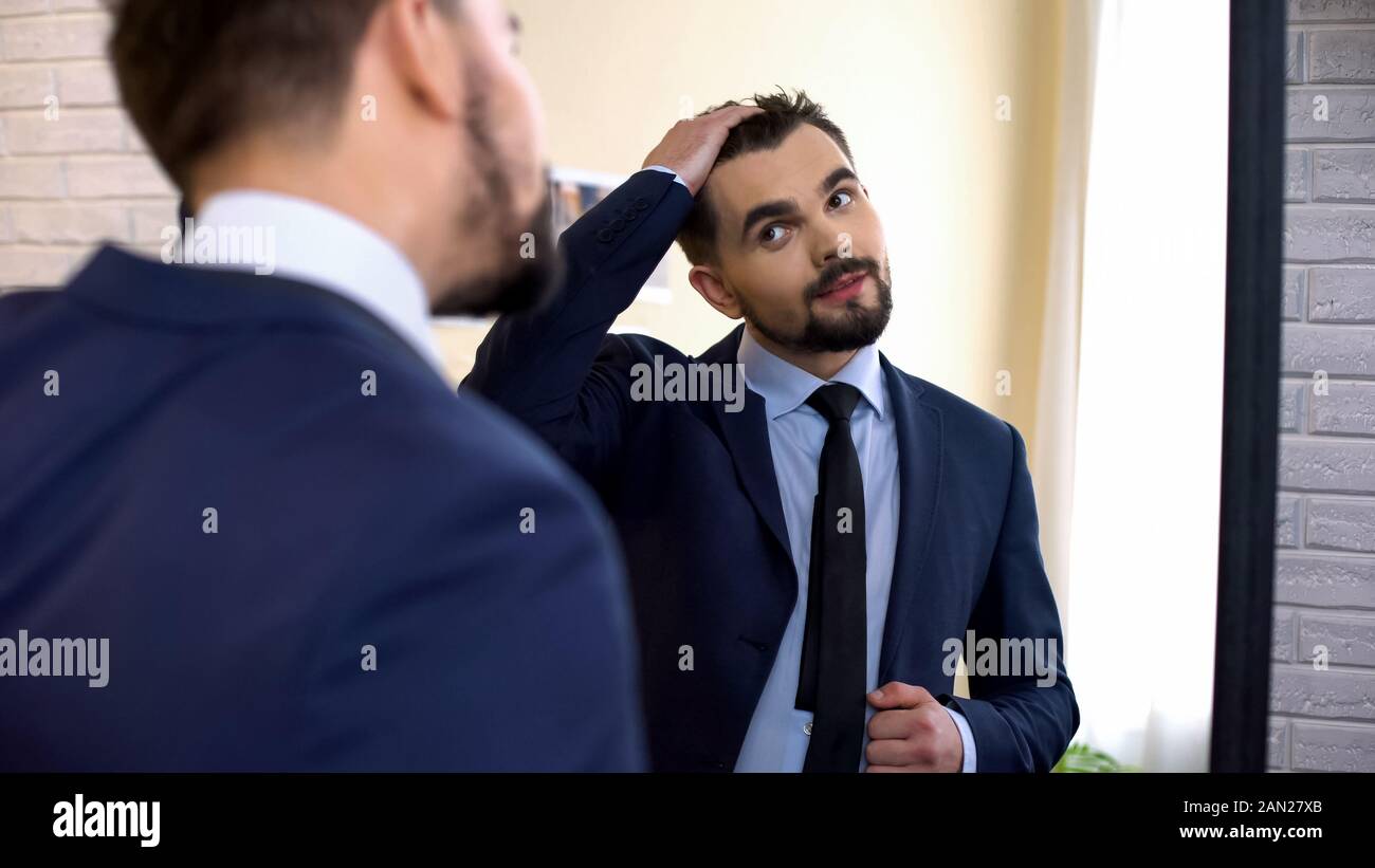 Junge Mitarbeiter in Anzug prüfen Haarschnitt in Spiegelbild Stockfoto