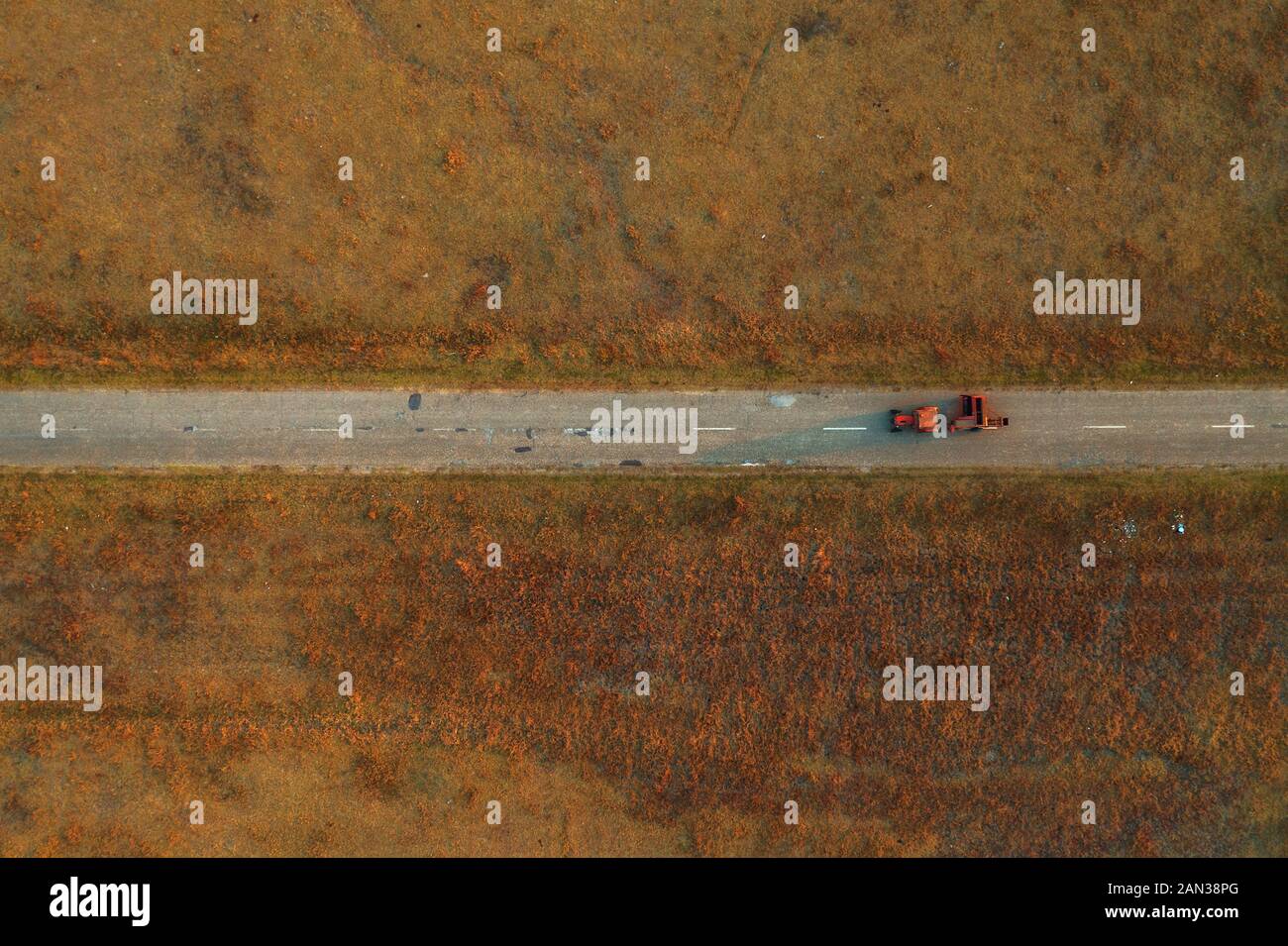 Alten Traktor auf abgenutzten asphaltierten Straße durch Graslandschaften Wiese, direkt oberhalb von Drone pov Stockfoto