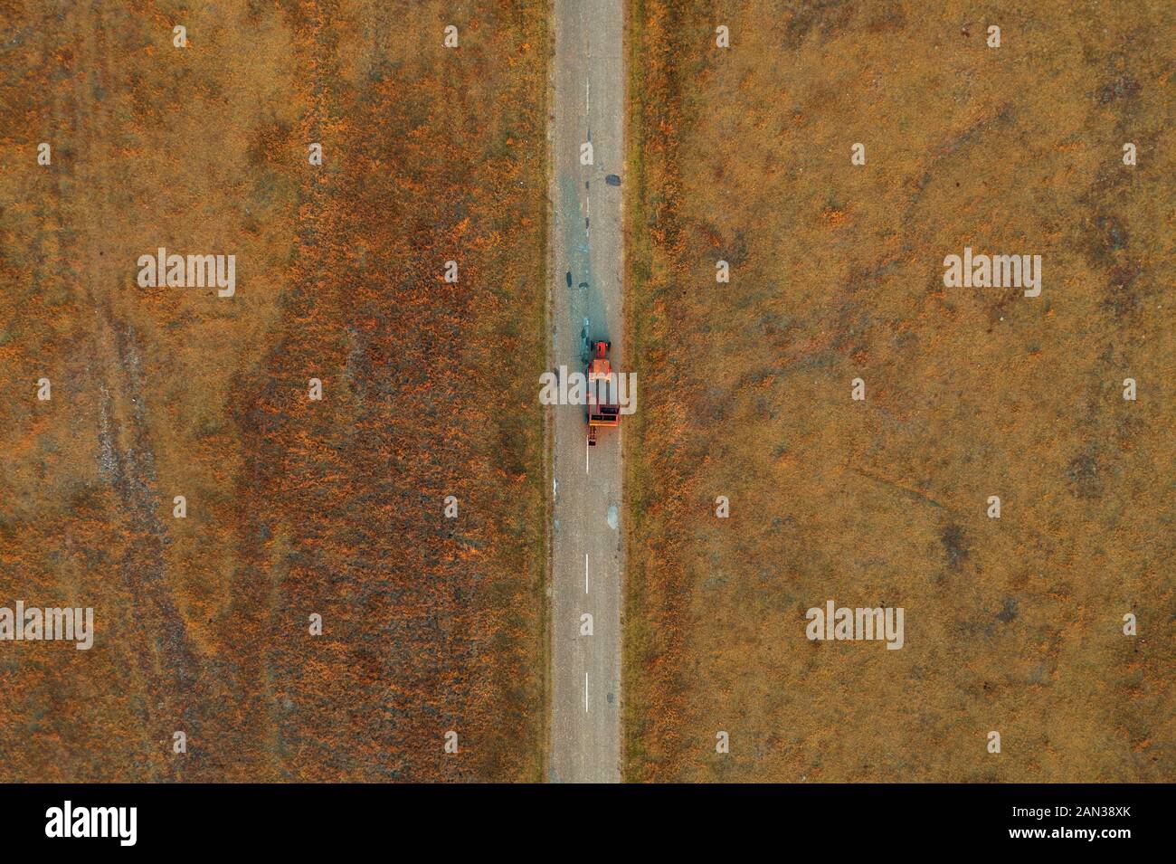 Alten Traktor auf abgenutzten asphaltierten Straße durch Graslandschaften Wiese, direkt oberhalb von Drone pov Stockfoto