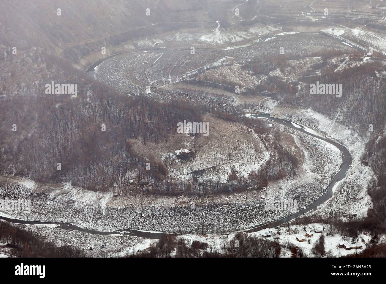 Schneebedeckte Häuser und Flöße am Ufer des mäandrierenden Zavoj-Sees, gefrorene Oberfläche, rote Herbstbäume am nebligen, nebligen Morgen Stockfoto