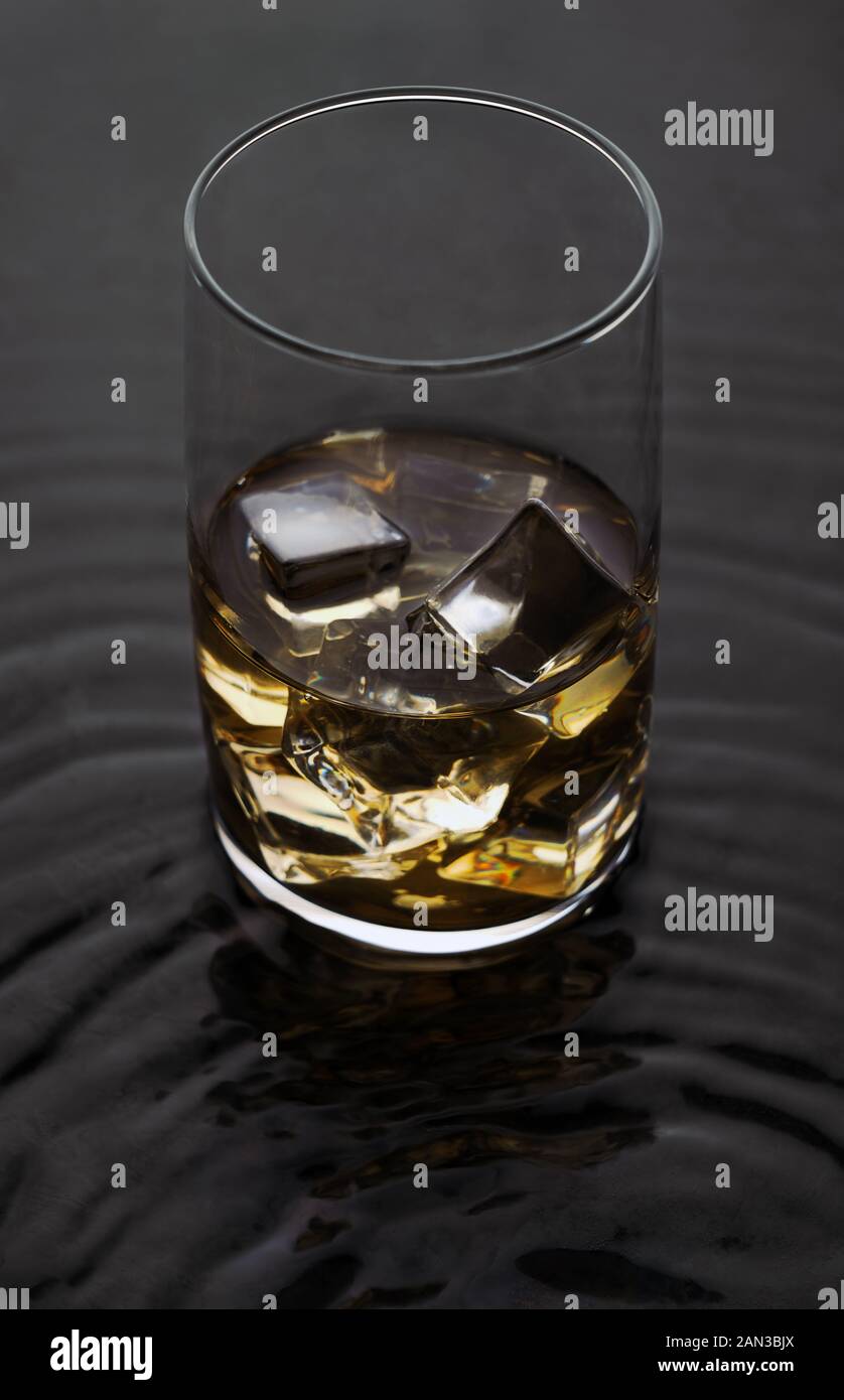 Whiskey Glas mit Eis auf Welligen flüssigen Oberfläche. Alkoholische Getränke mit Eiswürfeln auf nasser Oberfläche. Stockfoto