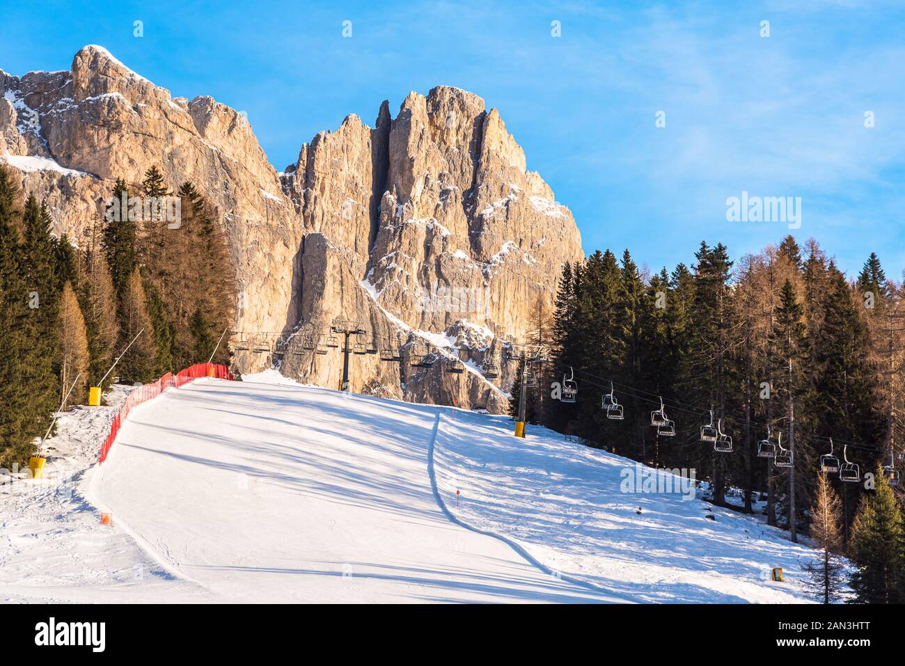 Leere Piste mit einem Sessellift im Hintergrund am Fuße des felsigen Gipfeln der Dolomiten an einem klaren Wintertag Stockfoto