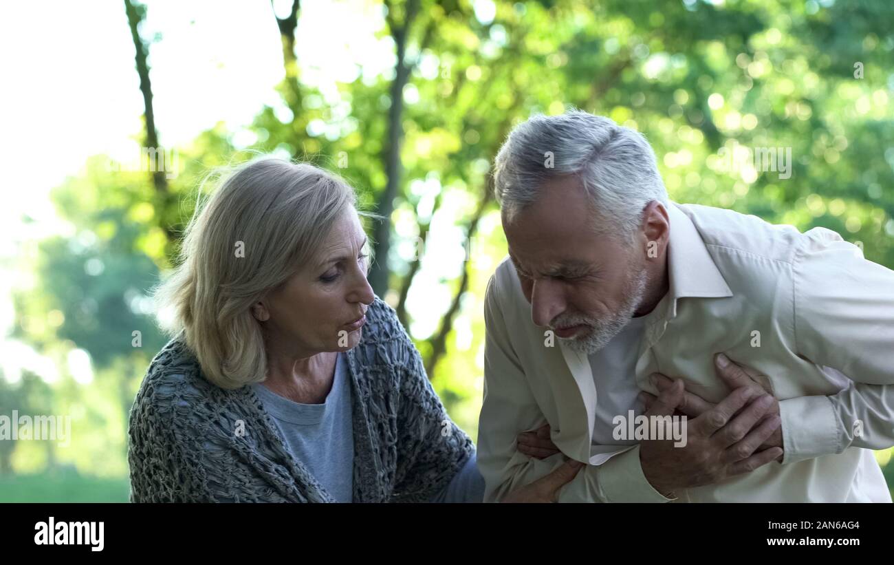 Alter Mann in plötzlichen Herzanfall beim Spaziergang im Park, Frau helfen ihm, Pflege Stockfoto