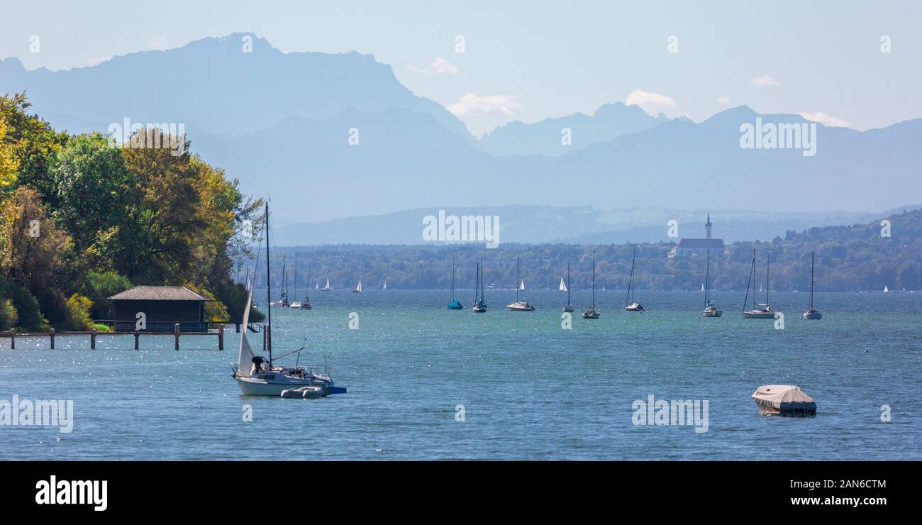 Panoramasicht auf den Ammersee - mit Segelbooten und einem Bootshaus im Vordergrund. Im hinteren Marienmuenster Diessen und die bayerischen alpen. Stockfoto
