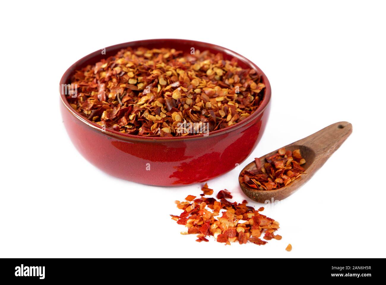 Hot Chili Flocken in einem roten Schüssel und Lose mit Löffel auf weißem Hintergrund Stockfoto