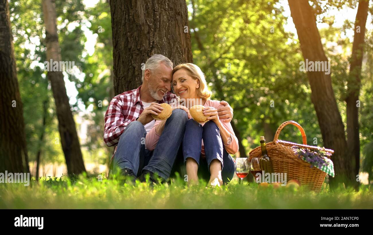 Freundliche alte Paar auf Gras und Burger essen, ausruhen, romantisches Date in Park Stockfoto
