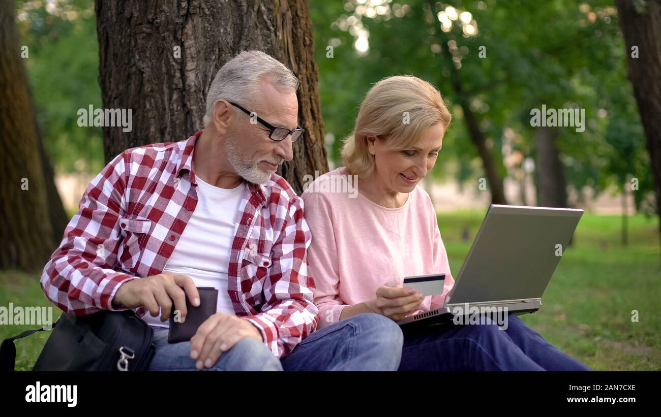 Glückliches Paar sitzt auf Gras und der Auswahl neuer Güter auf Laptop, online einkaufen Stockfoto