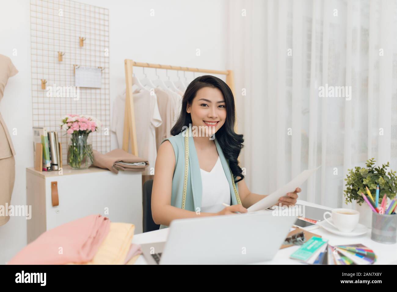 Glückliche junge asiatische Designer in der casualwear sitzen, Schreibtisch und Mode Skizzen Stockfoto