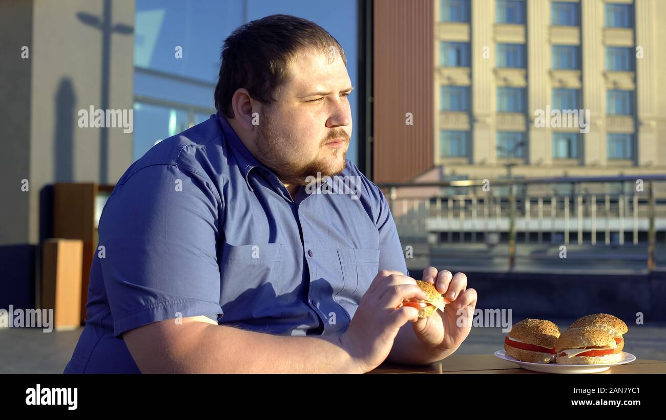 Nachdenklich beleibten Mann Burger essen, Zögern, neues Leben zu beginnen, Gewichtsverlust Stockfoto