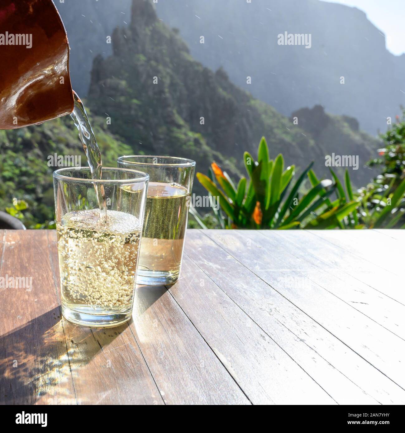 Man gießt Weißwein aus Ton Kanne in Glas auf der Terrasse mit Blick auf die grüne Landschaft der kleinen Bergdorf Masca auf Teneriffa, Spanien im sonnigen d Stockfoto