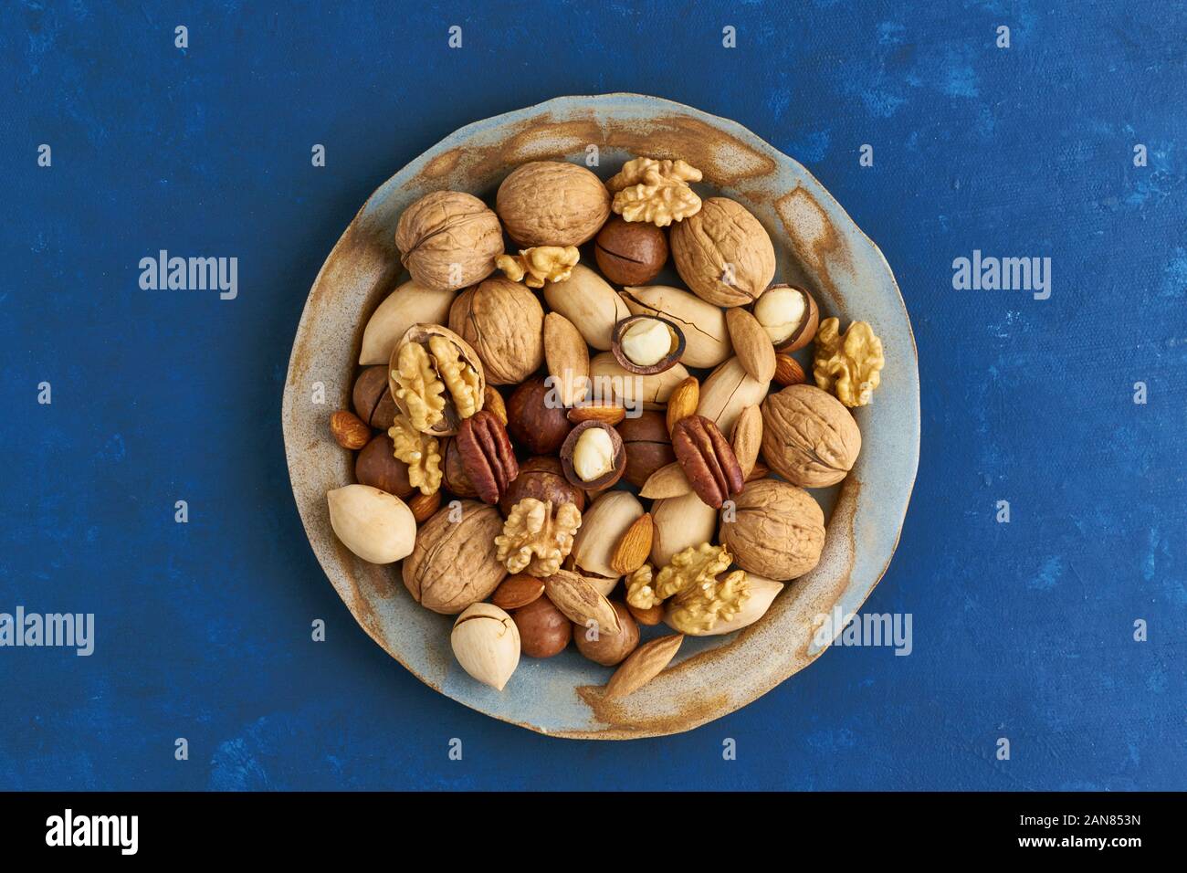 Classic blau in ein Lebensmittel. Mischung von Nüssen auf dem Teller - Walnuss, Mandeln, Pekannüsse, Macadamia und Messer zum Öffnen von Shell. Minimalismus. Gesund Vegan essen. Reinigen Sie e Stockfoto