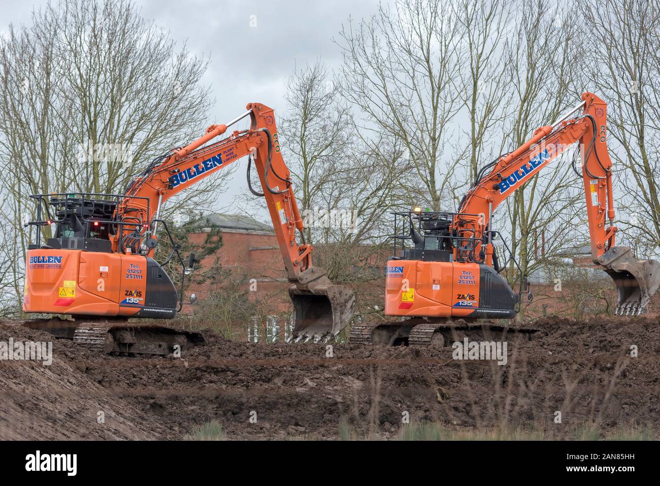 Wie Dinosaurier zwei Bagger bei der Arbeit auf der Baustelle. Name des Unternehmens Bullens. Stockfoto