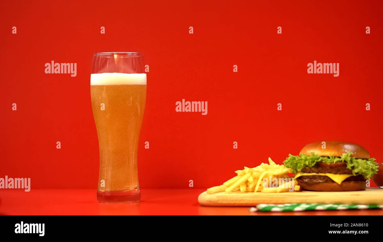 Bier mit Schaum und Hamburger auf roten Hintergrund, Kohlenhydrate und Fette Speisen Stockfoto