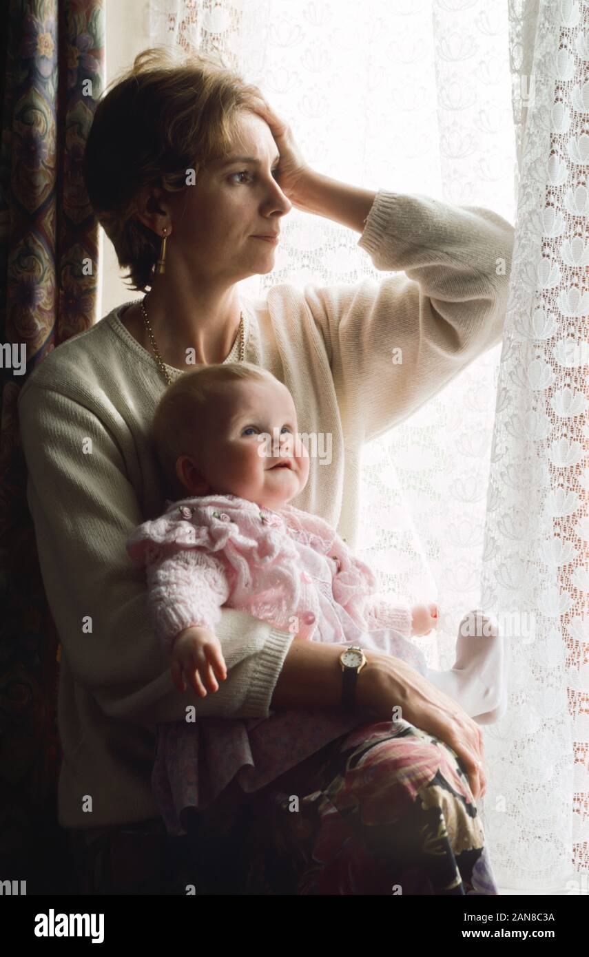 Junge Mutter leiden von postnatalen Depressionen, mit ihrem Baby neben Terrassentüren sitzen, die gerne ausserhalb traurig Stockfoto