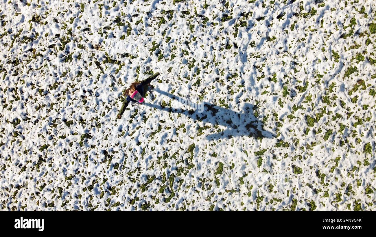 Luftaufnahme von einem Mädchen auf einer Rasenfläche mit Schnee bedeckt und verbreitet ihren Arm und das Betrachten der eigenen Schatten. Ansicht von oben von einer Drohne Stockfoto