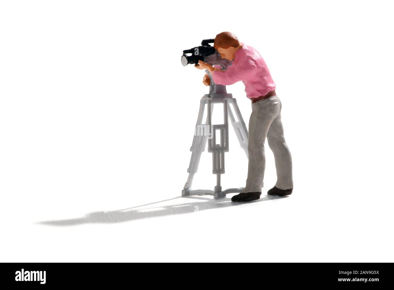 Miniatur Kameramann arbeiten mit TV-Kamera auf einem Stativ, schießen eine Szene. Kleine Person isoliert auf auf weißem Hintergrund mit langen Schatten Stockfoto