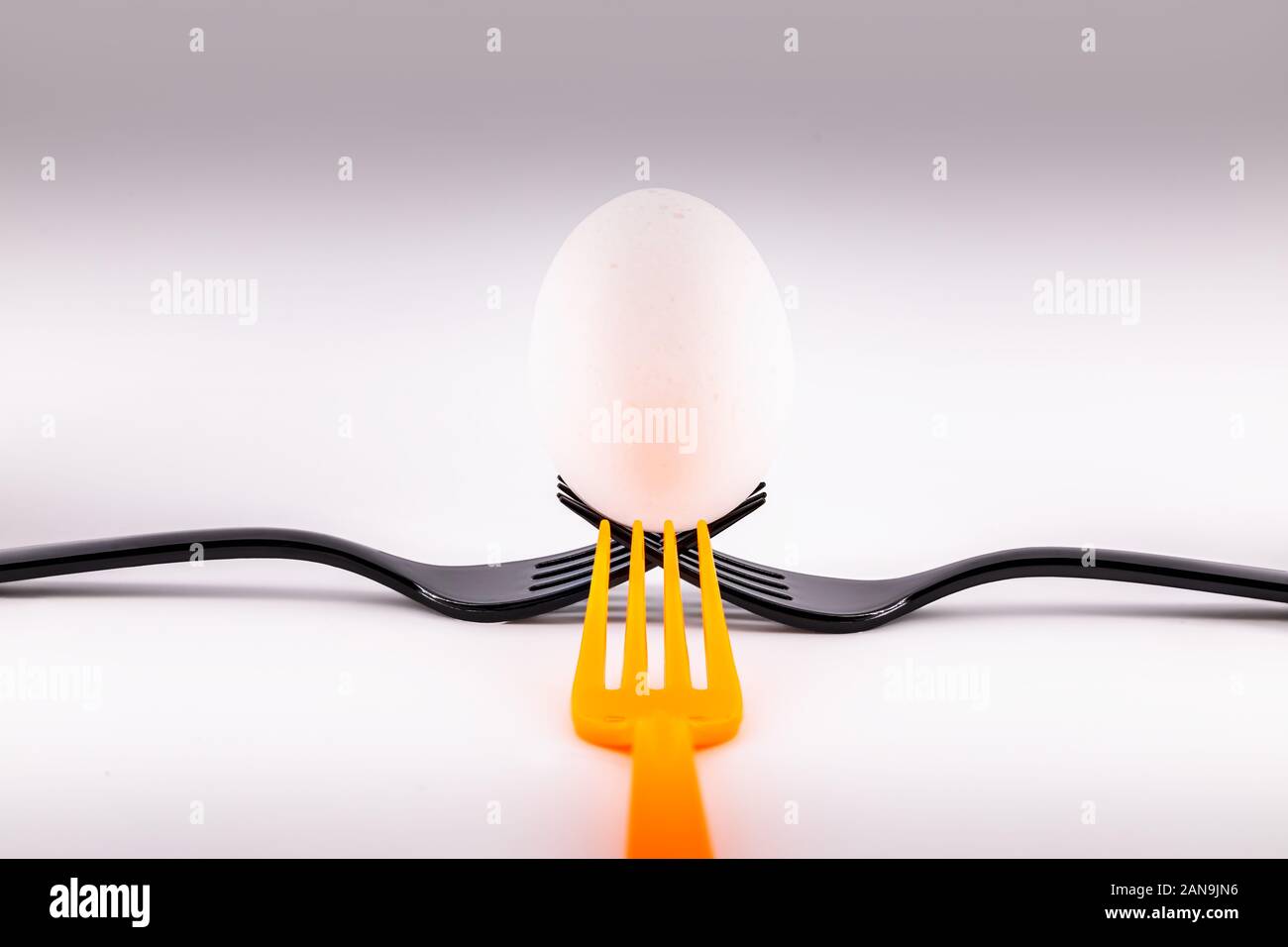 Zwei schwarze Gabeln und eine orange Gabel Holding ein Ei. Konzept einschließenden Teamarbeit Stockfoto