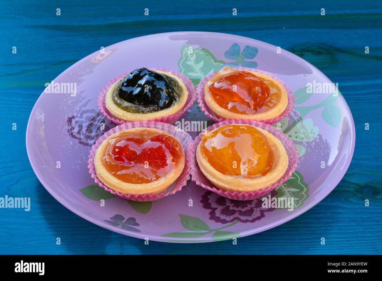 Körbchen des Teigs in mit verschiedenen kandierten Früchten gefüllt, in rosa Glasplatte auf Blau Holztisch serviert. Stockfoto