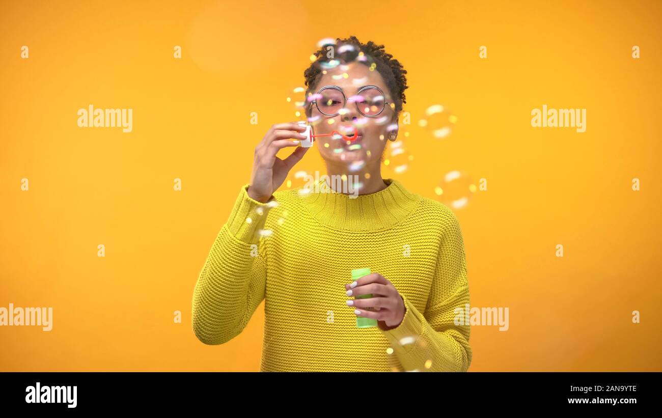 Freudige schwarze Frau bläst Seifenblasen auf gelbem Hintergrund, Jugend Glück Stockfoto