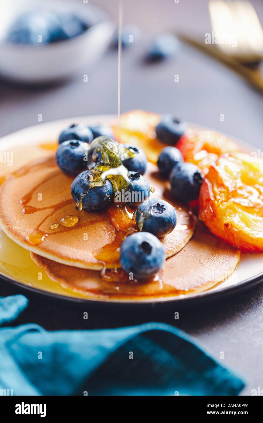 Gießen Honig auf Pfannkuchen mit gegrillte Pfirsiche und frische Heidelbeeren. Stockfoto