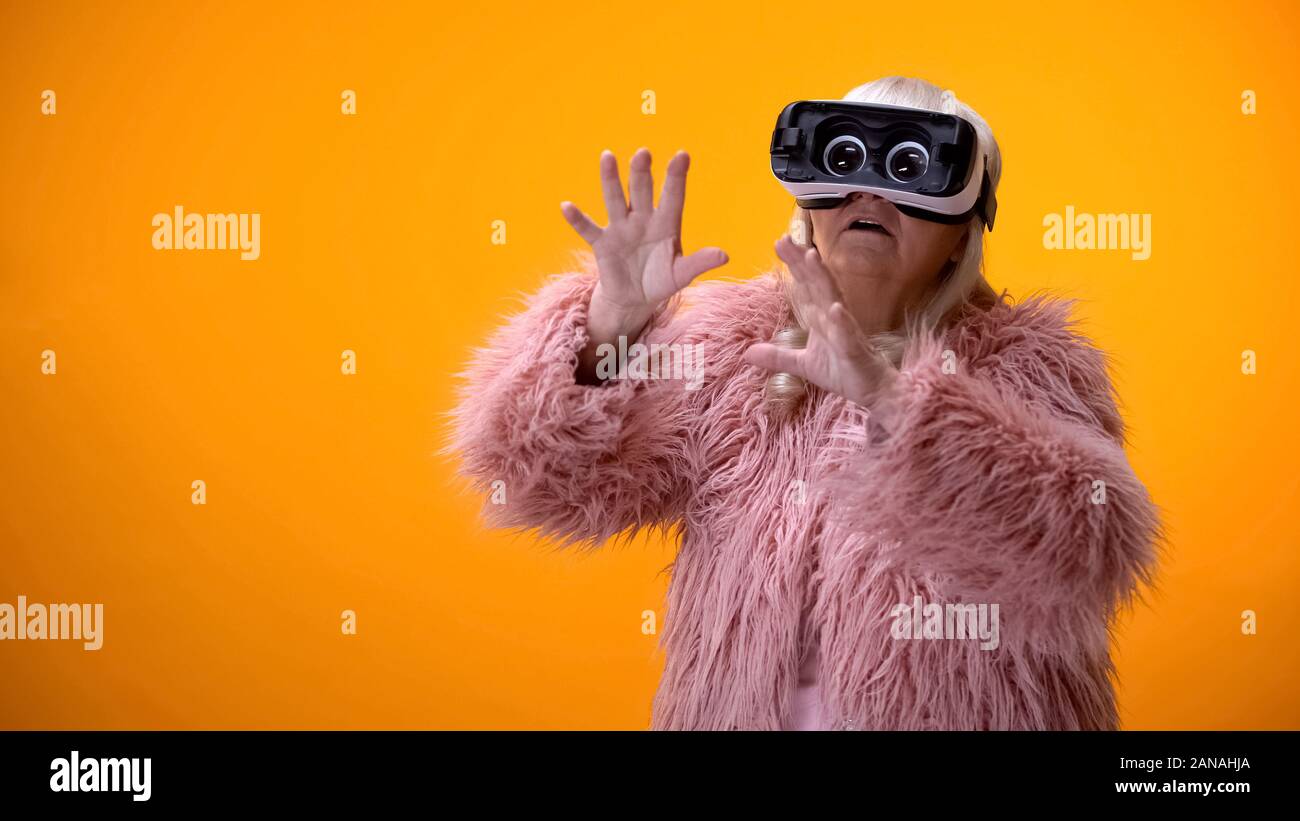 Ältere Frau in lustig Fell und VR-Headset spielen video game, Hi-end Innovationen Stockfoto