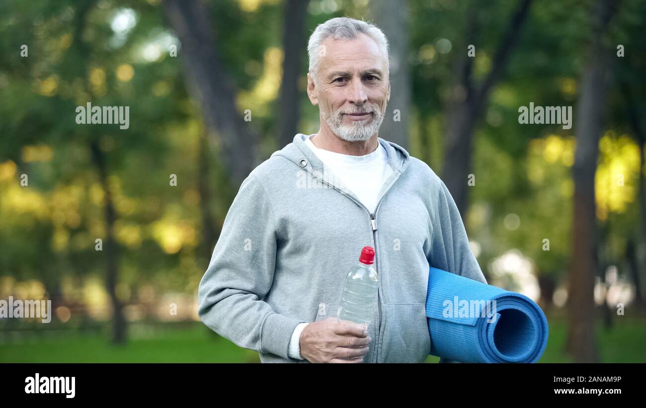 Bart Großvater in Sportkleidung holding Yoga Matte und einer Flasche Wasser, Gesundheit Stockfoto