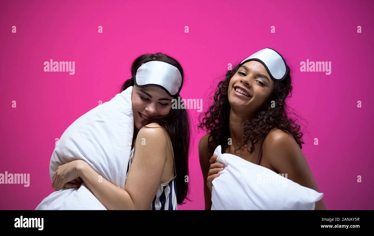 Zwei Frauen in Schlafanzug und Augenmasken tanzen mit Kissen, Spaß im Innenbereich Stockfoto